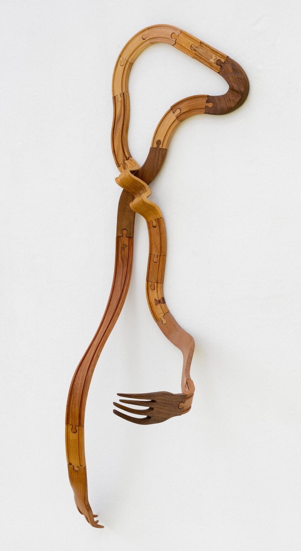 an abstract, wooden wall sculpture resembling a long, twisted fork