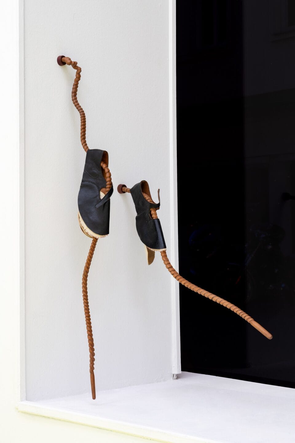 an abstract sculpture made primarily of wood, showing two tendrils attached to a wall with shoes on each one