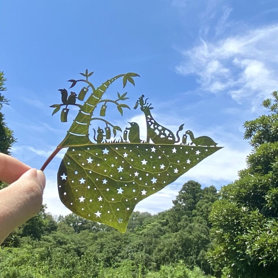 a cut leaf artwork of a giraffe and a bird by a tree