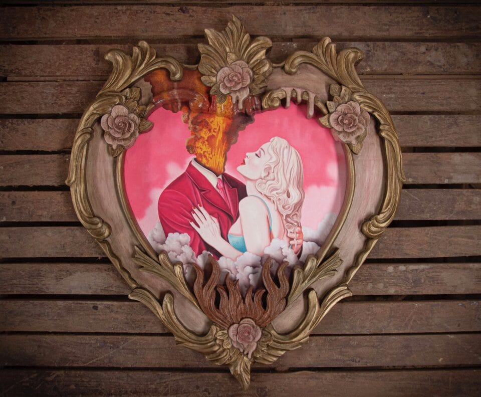 a heart-shaped portrait, framed with an ornate wooden frame, of a woman embracing a man whose head is exploding with fire