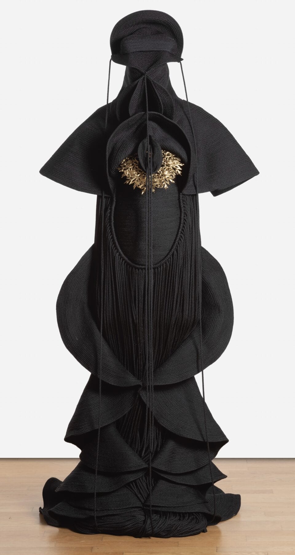 a sculpture made from black cord, thread, and metal in the form of a figure or long, dramatic garment